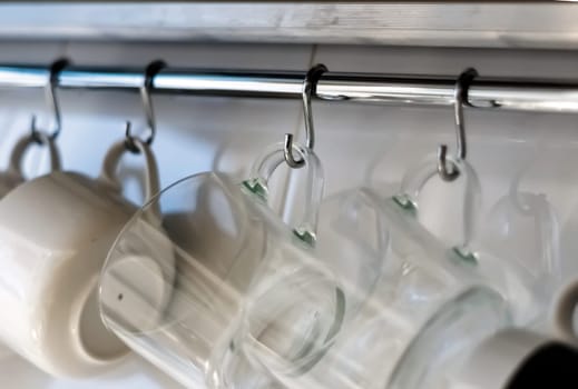 A set of mugs hanging on hooks in a modern home kitchen. Everyday objects. Domestic life.