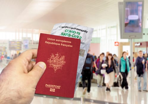 hand holding a french passport with a wrinkled paper Coronavirus Covid 19 immunity certificate. Blurred airport in the background. Immunity from Covid-19. Travel without restrictions in the EU Union