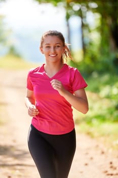 woman enjoying in a healthy lifestyle while jogging on a country road through the beautiful sunny forest, exercise and fitness concept
