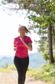 woman enjoying in a healthy lifestyle while jogging on a country road through the beautiful sunny forest, exercise and fitness concept