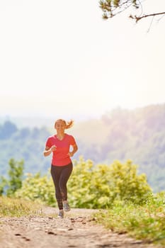 woman enjoying in a healthy lifestyle while jogging on a country road through the beautiful sunny forest, exercise and fitness concept