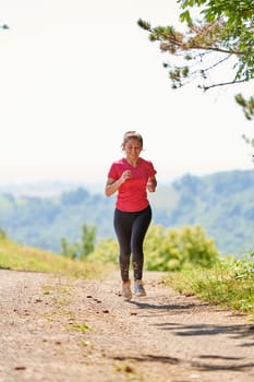 woman enjoying in a healthy lifestyle while jogging on a country road through the beautiful sunny forest, exercise and fitness concept