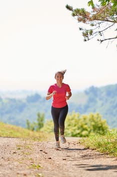 woman enjoying in a healthy lifestyle while jogging on a country road through the beautiful sunny forest, exercise and fitness concept