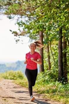 woman enjoying in a healthy lifestyle while jogging on a country road through the beautiful sunny forest, exercise and fitness concept