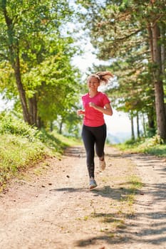 woman enjoying in a healthy lifestyle while jogging on a country road through the beautiful sunny forest, exercise and fitness concept