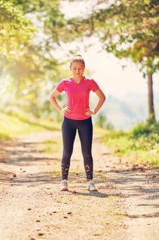 woman enjoying in a healthy lifestyle while jogging on a country road through the beautiful sunny forest, exercise and fitness concept