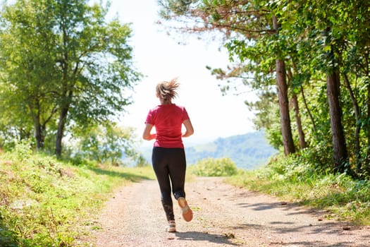 woman enjoying in a healthy lifestyle while jogging on a country road through the beautiful sunny forest, exercise and fitness concept
