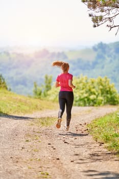 woman enjoying in a healthy lifestyle while jogging on a country road through the beautiful sunny forest, exercise and fitness concept