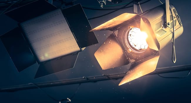 Professional orange studio spotlight hanging on the ceiling. Lighted dust particles and lens flares.