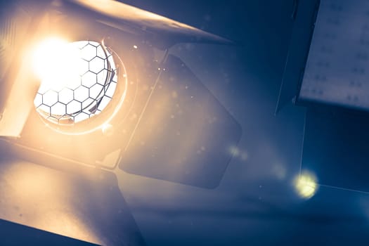 Professional orange studio spotlight hanging on the ceiling. Lighted dust particles and lens flares.