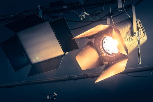 Professional orange studio spotlight hanging on the ceiling. Lighted dust particles and lens flares.