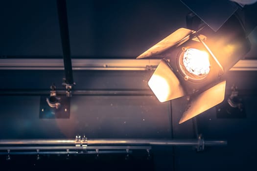 Professional orange studio spotlight hanging on the ceiling. Lighted dust particles and lens flares.