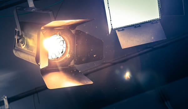 Professional orange studio spotlight hanging on the ceiling. Lighted dust particles and lens flares.
