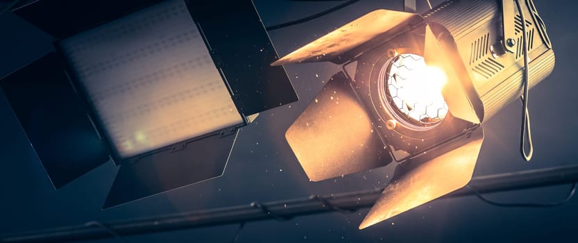 Professional orange studio spotlight hanging on the ceiling. Lighted dust particles and lens flares.