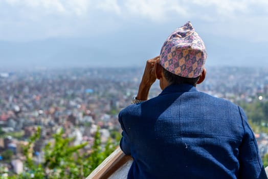 KATHMANDU, NEPAL - CIRCA MARCH 2015: Nepali man wearing a topi contemplates Kathmandu city from Swayambhunath.