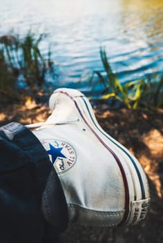 BIARRITZ, FRANCE - CIRCA APRIL 2021: Worn white Converse Chuck Taylor All Star sneaker, lake shore in the background.