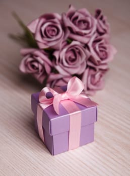 violet roses and gift box with pink ribbon on wooden surface
