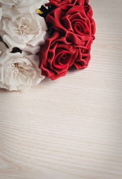 artificial bouquet of red and white roses on wooden surface with space for text