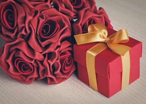 red gift box and red roses on wooden surface