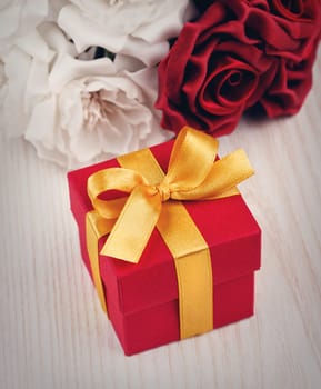 red and white roses and red gift box with yellow ribbon on wooden surface