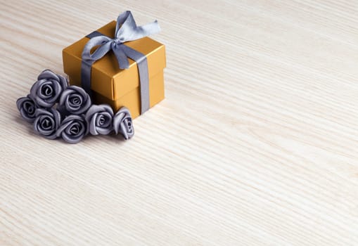 grey flowers and golden gift box with ribbon on wooden surface with space for text