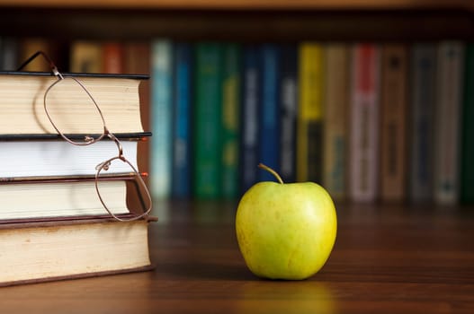 green apple on the table with books and glasses