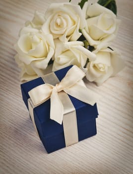 blue gift box with white roses on wooden surface