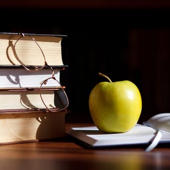 green apple on the open book with books and glass