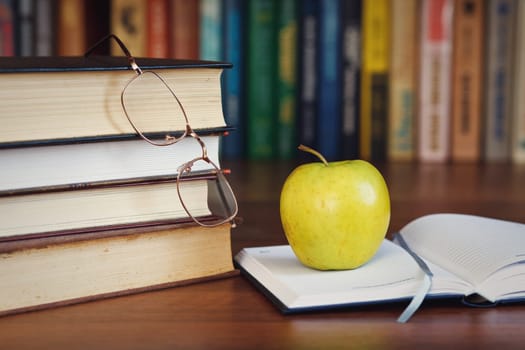green apple on the open book with books and glasses