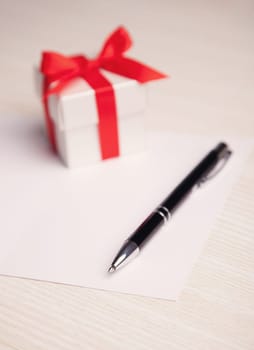 Blank card, pen and white gift box with red ribbon