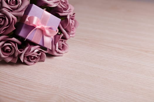 purple roses and gift box with pink ribbon on wooden surface with space for text