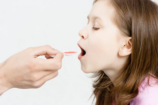 Treatment of the child. Girl is drinking red medicinal syrup