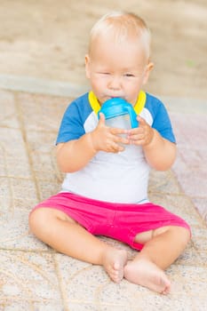 Cute baby sitting on a sand and drinking