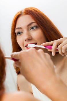 Attractive young woman in the morning brushing her teeth in the mirror in the bathroom with long red hair