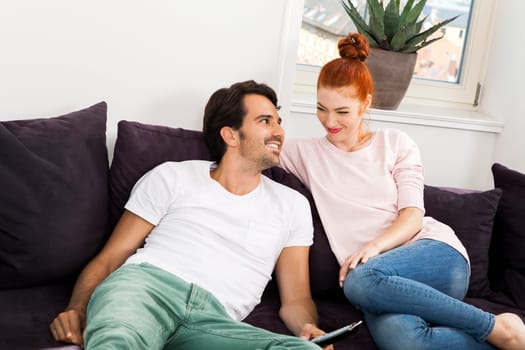 Happy young couple sit at home in the living room on the couch and cuddle in love