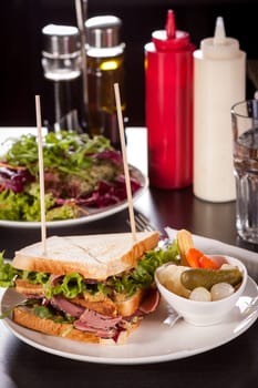 Delicious sandwich clubsandwich with bacon ham cheese and one with mixed pickels on a plate