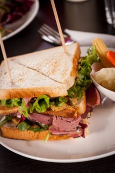 Delicious sandwich clubsandwich with bacon ham cheese and one with mixed pickels on a plate