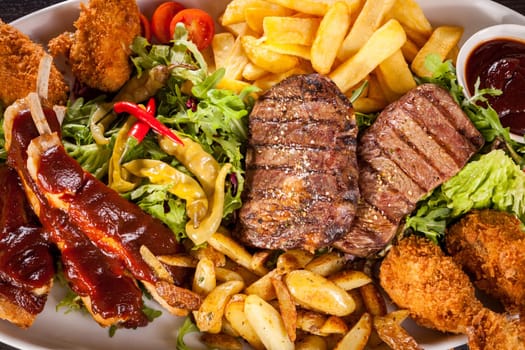 Huge barbecue plate with mixed meat and steaks on salad
