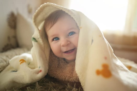 Smiling baby girl crawling on bed under the blanket. Adorable kid portrait. 6 month old child. Childhood concept. High quality photo