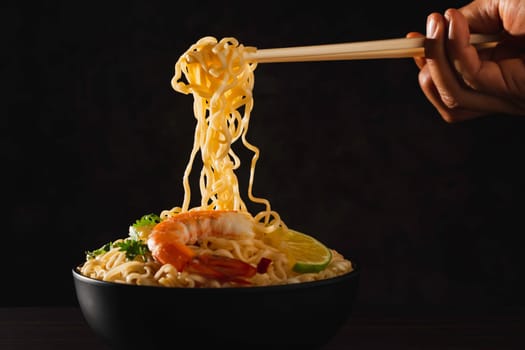 Hand using chopsticks pickup instant noodles with smokes isolated on black background.