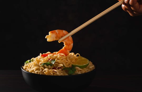 Hand using chopsticks pickup instant noodles with smokes isolated on black background.