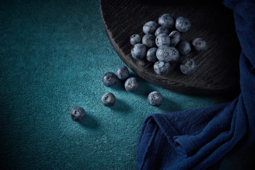 Ripe blueberries (bog whortleberry, great bilberry) on black wooden board on dark blue background. Top view
