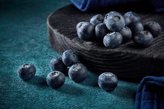 Ripe blueberries (bog whortleberry, great bilberry) on black wooden board on dark blue background.