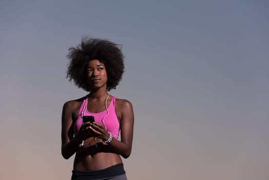 portrait of a young beautiful african american woman with headphones and mobile phone jogging in nature beautiful summer night