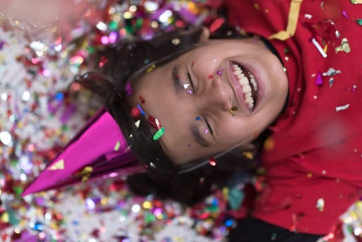 Happy kid celebrating party with blowing confetti while lying on the floor