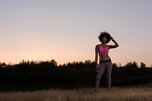 portrait of a young beautiful african american woman with headphones and mobile phone jogging in nature beautiful summer night
