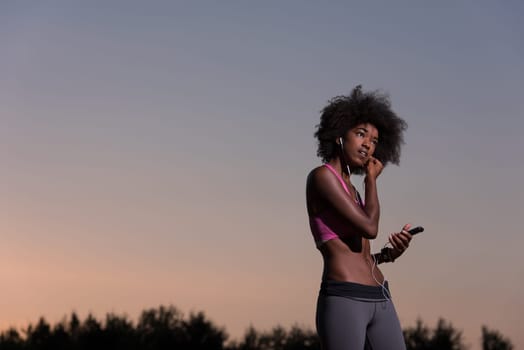 portrait of a young beautiful african american woman with headphones and mobile phone jogging in nature beautiful summer night