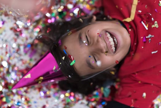 Happy kid celebrating party with blowing confetti while lying on the floor