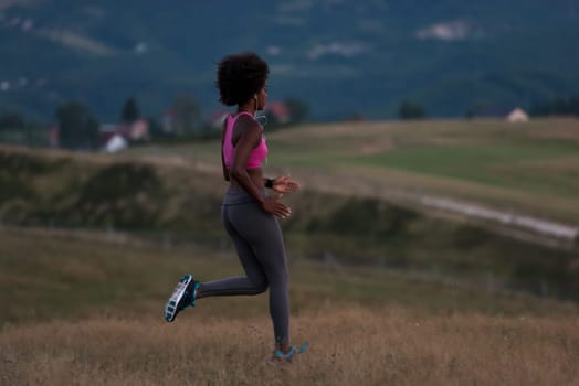 young African american woman runner with headphones jogging outdoors in nature beautiful summer night - Fitness, people and healthy lifestyle