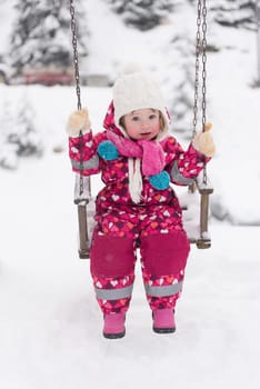 child outdoor in park at winter day with fresh snow, cute little girl swing and playing